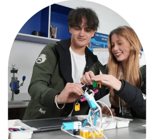 Dos jóvenes estudiantes, un hombre y una mujer, trabajando en equipo para ensamblar un prototipo de robótica en el aula.